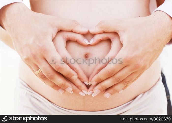 A couple making a heart shape on the pregnant belly with their hands. Concept of pregnancy, expecting a baby, love, care.