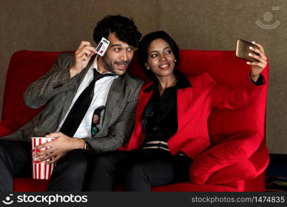 A couple man and woman take a photo with a ticket while sitting and waiting In front of the cinema