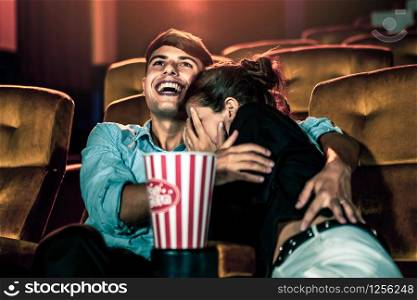 A couple of caucasian watch a thriller movie in the cinema, woman eyes closed and turning her face away from the screen