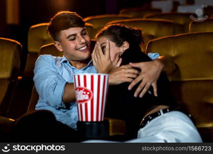 A couple of caucasian watch a thriller movie in the cinema, woman eyes closed and turning her face away from the screen