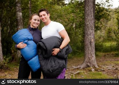 A couple of happy campers standing with sleeping bags