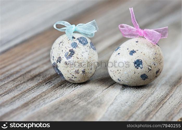 A couple of quail eggs with blue and pink bows on the background of the old wooden boards