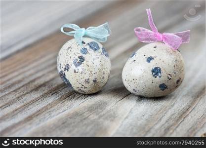 A couple of quail eggs with blue and pink bows on the background of the old wooden boards