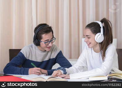 A couple of smiling teenagers have fun while reading a book and listening to a lesson on their headphones on an out of focus background. Student concept.. A couple of teenagers working on a project
