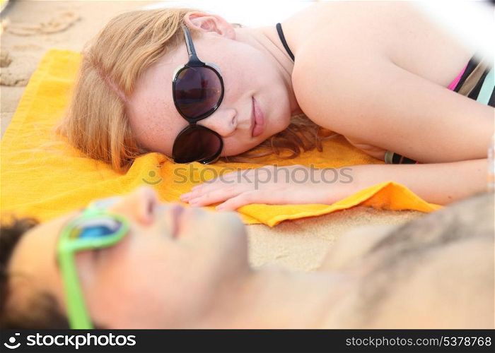 A couple of teenagers sleeping on the beach.