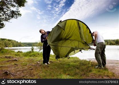 A couple setting up a tent in the forest by a lake