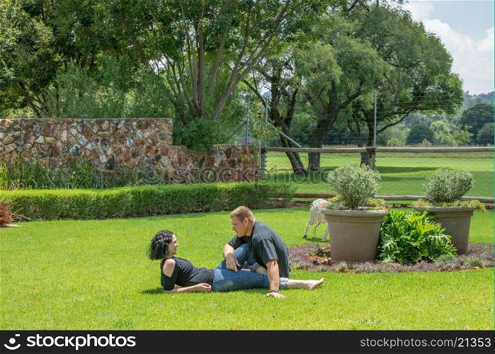 A couple sit on the lawn in their garden enjoying the nice summer weather, while chatting to each other.