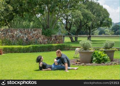 A couple sit on the lawn in their garden enjoying the nice summer weather, while chatting to each other.