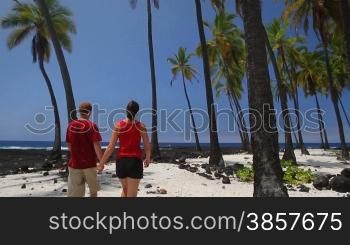 A couple walks into frame at a beautiful palm tree shore in Hawaii