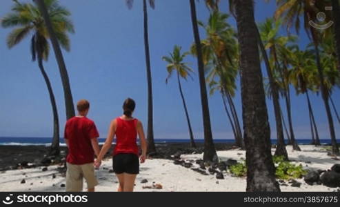 A couple walks into frame at a beautiful palm tree shore in Hawaii