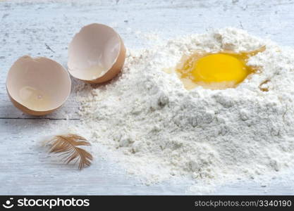 A Cracked Egg In Some Flour, With The Shell and A Hen Feather To The Side