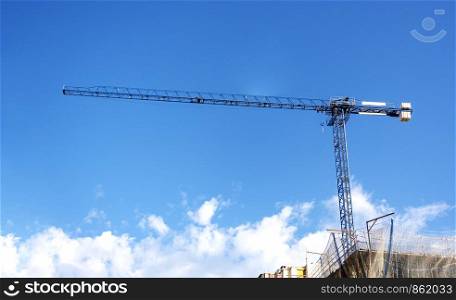 a crane lifting weights on a construction site with a blue sky and clouds on the background. construction and construction engineering.