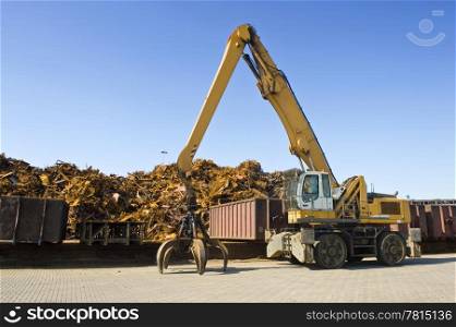 A crane with a huge claw in front of a steel scrap heap