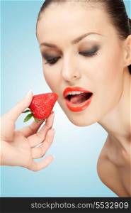A creative portrait of a beautiful girl being fed with a red ripe strawberry.
