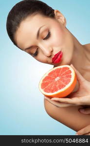 A creative portrait of a beautiful girl holding a red grapefruit sexually under her chin.