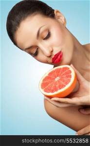 A creative portrait of a beautiful girl holding a red grapefruit sexually under her chin.