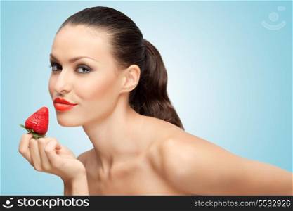 A creative portrait of a beautiful girl holding with one hand a juicy strawberry near her lips with temptation.