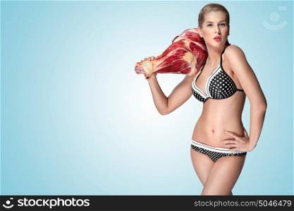 A creative portrait of a beautiful girl in bikini holding raw meat on her shoulder.