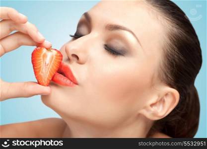 A creative portrait of a beautiful girl kissing a fresh strawberry with delicious red lips.