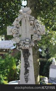 A cross gravestone decorated with a stone flower wreath