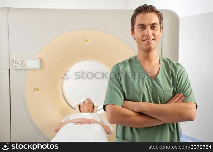 A CT scanner technician standing infront of a CT Scanner with a patient