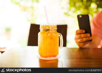 A cup full of fresh orange juice with cocktail straw on wooden table. Man is doing mobile photography. Fresh orange pleasure