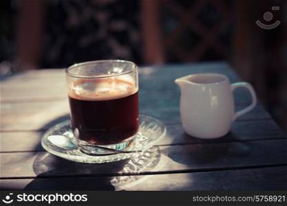 A cup of black coffee on a table in the sunlight