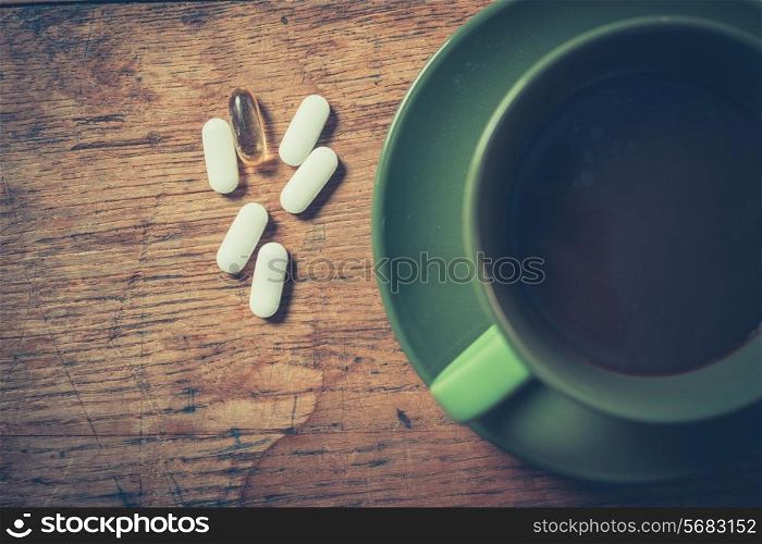 A cup of black coffee with six pills next to it