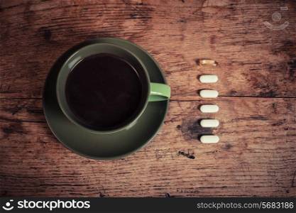 A cup of black coffee with six pills next to it