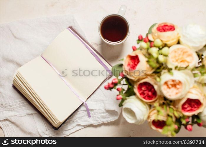 A cup of black tea, notebook and beautiful flowers on the table, top view. The concept of inspiration to creativity. Inspiration for solving difficult problems