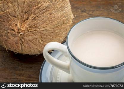 a cup of coconut milk with a coconut against wood background