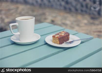 A cup of coffee and a piece of cake on a table outside