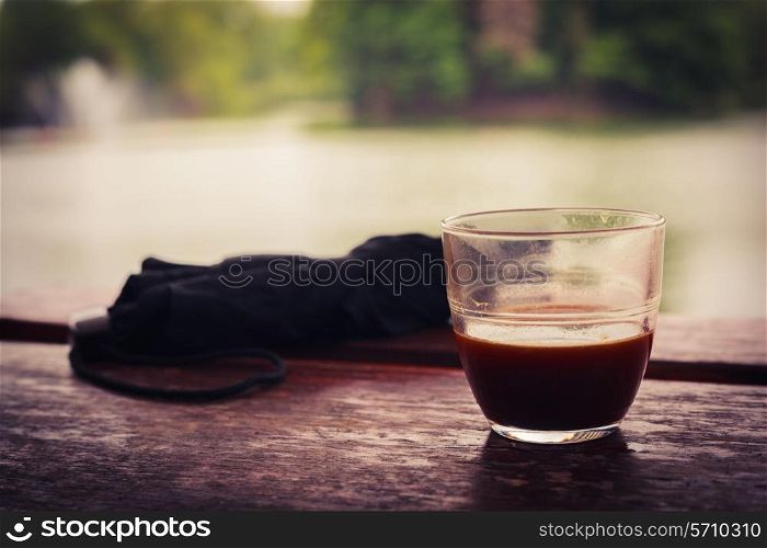 A cup of coffee and an umbrella on a wooden table by a lake in the afternoon