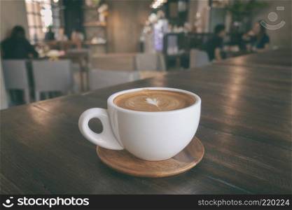 A cup of coffee latte on wooden table in warm cafeteria