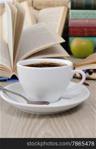 A cup of coffee on the table against the background of an open book with a notebook