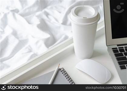 A cup of coffee puts beside laptop computer and mouse with white tray on messy blanket for working on bed concept.