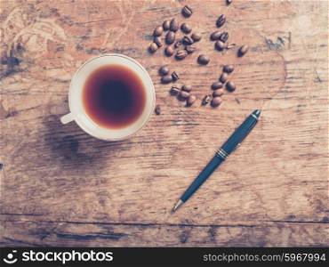 A cup of coffee with beans and a pen on a wooden table