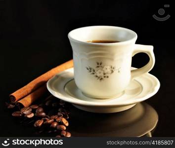 a cup of coffee with cinnamon sticks on black background