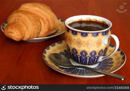 A cup of coffee with croissant. Shallow depth of field. Focus on the cup.
