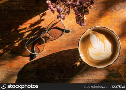 A cup of coffee with latte art and glasses on wooden table in coffee shop, top view.