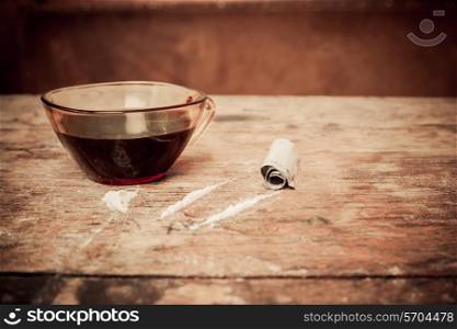 A cup of coffee with lines of cocaine and a rolled up banknote next to it
