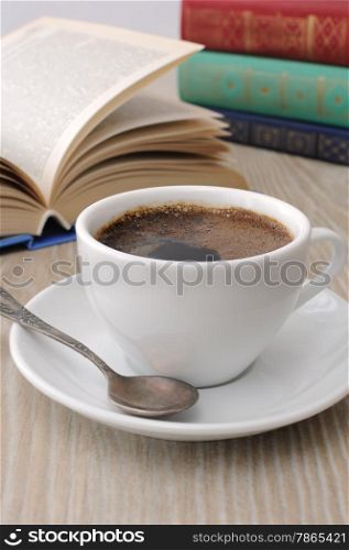A cup of fragrant black coffee on the table against the background of an open book
