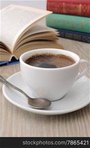 A cup of fragrant black coffee on the table against the background of an open book
