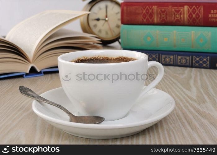 A cup of fragrant black coffee on the table against the background of an open book&#xA;&#xA;