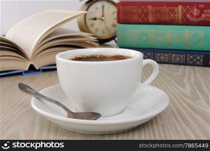 A cup of fragrant black coffee on the table against the background of an open book&#xA;&#xA;