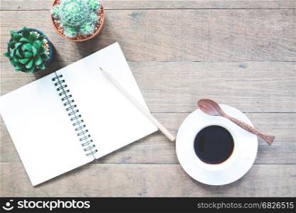 A cup of hot coffee with empty notebook and pot of cactus on wooden table with copy space