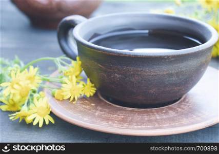 A cup of tea from yellow daisies with a bouquet of daisies on a wooden background. Close-up.. A cup of tea from yellow daisies with a bouquet of daisies on a wooden background.