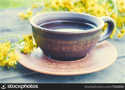A cup of tea from yellow daisies with a bouquet of daisies on a wooden background. Close-up.. A cup of tea from yellow daisies with a bouquet of daisies on a wooden background.