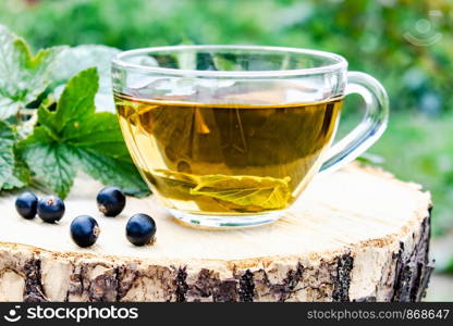 A cup of tea with black currant leaves. Tea with currants on a wooden table in the open air. Close-up.. A cup of tea with black currant leaves. Tea with currants on a wooden table in the open air.