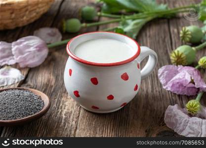 A cup of vegan milk made from ripe poppy seeds, with fresh unripe plant in the background